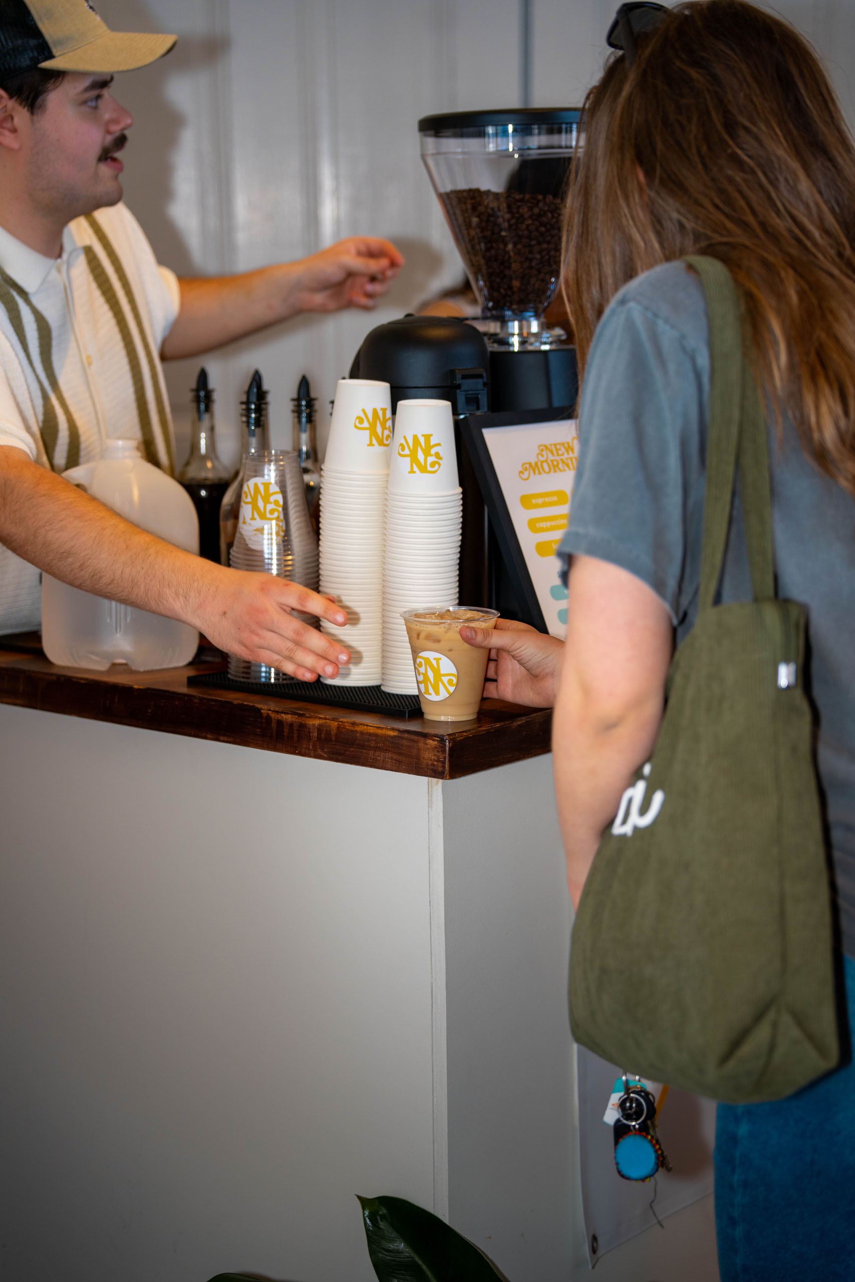 A guest receiving a handcrafted iced coffee from the New Mornings Coffee cart, with branded cups and a menu board visible in the background